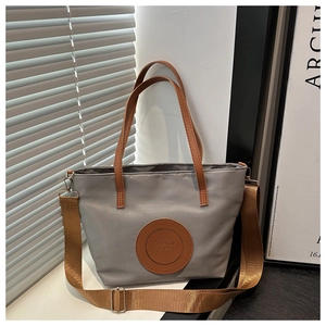 Detail view of grey nylon tote bag with brown leather handles and adjustable shoulder strap
