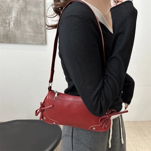 Red shoulder bag with bow accents and silver studs worn by a model in a minimalist setting