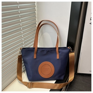 Detail of navy nylon tote bag showing brown leather logo patch and metal zipper closure