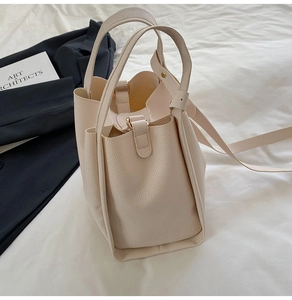 Detail view of cream bucket bag in lychee leather with shoulder strap and top handle