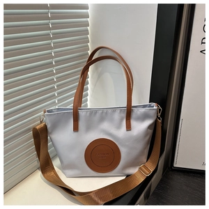 Close-up of blue nylon tote with brown leather handles and adjustable shoulder strap
