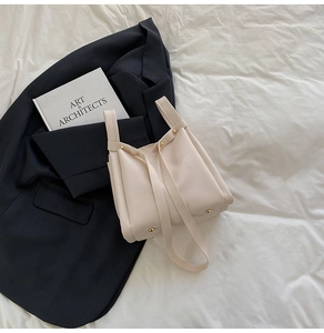 Detail of cream lychee leather bucket bag with gold rivets on textured white background