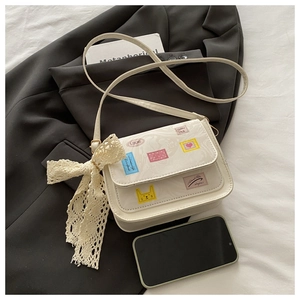 Detail of off-white tote bag featuring colorful stamp patches and a large lace bow accent