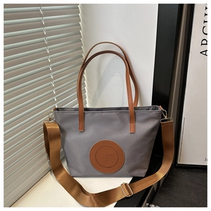 Detail of grey waterproof nylon tote bag with fashion logo patch and brown fabric strap
