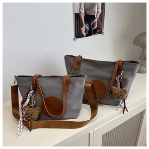 Detailed macro view of gray nylon tote bags with brown faux leather handles and bear charms