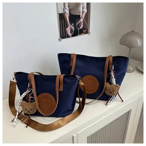 Detail of navy nylon tote bags with brown leather handles and bear charm in lifestyle setting