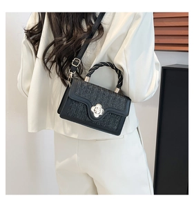 Detail of black woven crossbody bag with golden clover clasp worn by a model