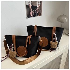 Detail of black nylon tote bags with brown leather handles and plush bear pendants
