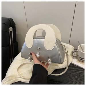 Gros plan du sac coquillage argenté avec perles et poignée blanche tenu à la main