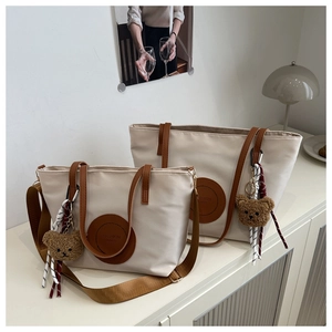 Detail showing large and small nylon tote bags with brown handles and teddy bear charm