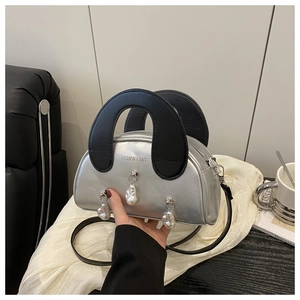 Détail du sac coquille argenté avec large poignée noire et pendentifs en perles