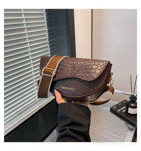 Detail of dark brown saddle bag featuring woven texture and adjustable wide shoulder strap