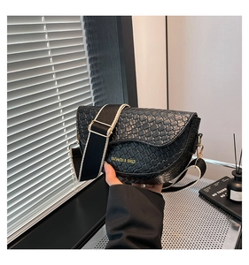 Detail of black woven texture saddle bag with wide canvas strap and gold lettering