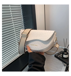 Close-up of white half-moon saddle bag with embossed woven texture and wide strap