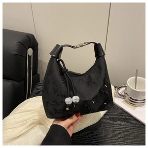 Détail d'un sac à main noir en tissu avec nœud 3D, glands perlés et poignée en cuir sur table