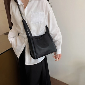 Minimalist black pebble leather bucket bag with adjustable strap and metal feet on base