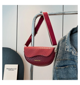 Close-up of red woven saddle bag featuring a wide strap and gold fashion lettering