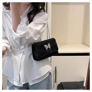 Detail of black pleated crossbody bag with silver butterfly buckle and chain strap