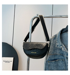 Detail of black crocodile texture saddle bag with chic woven strap and gold hardware