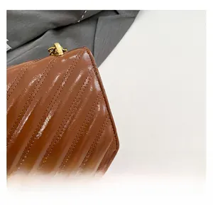 Detail of brown quilted leather bag featuring diagonal stitching and golden metal chain