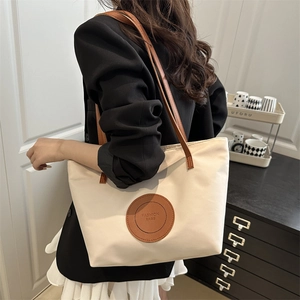 Minimalist beige nylon tote bag with brown straps styled on a model in a modern room