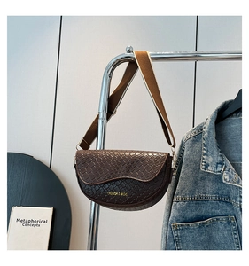 Detail of dark brown woven saddle bag with wide strap and golden fashion lettering