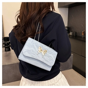 Detail of light blue crossbody bag with crinkled texture and golden butterfly clasp