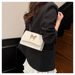 Close-up of white patent leather shoulder bag with silver butterfly and chain strap