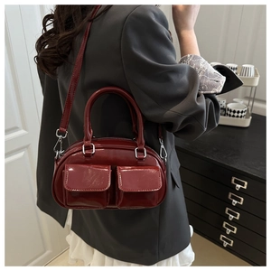 Close-up of a glossy burgundy crossbody bag featuring dual front pockets and silver zippers