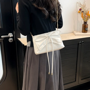 White ballet style shoulder bag with bow and gold chain strap shown on a model