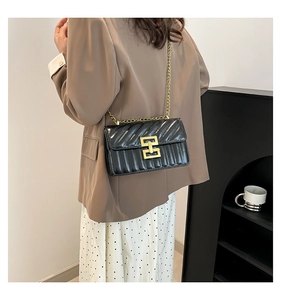 Close-up of black quilted small square bag with elegant gold geometric metal buckle and chain