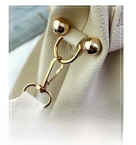 Detail of golden lobster clasp hardware and lychee pattern leather on a white bucket bag
