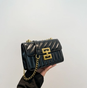 Detail of black quilted chain bag featuring V-shaped stitching and golden geometric lock