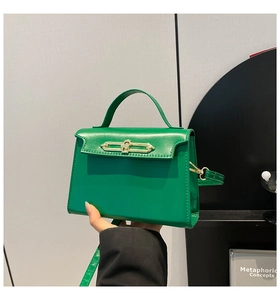 Detail of green leather handbag with golden buckle lock and top handle held by a model