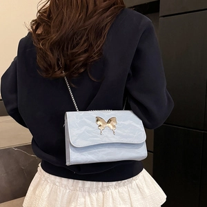 Light blue chain flap bag with large butterfly clasp worn by a model in casual style