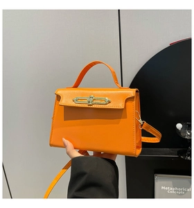 Detail of elegant orange leather handbag with golden metal buckle and top handle