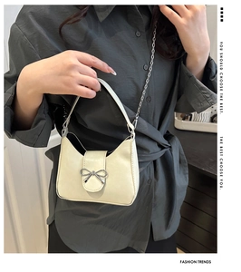 Detail of a creamy white crossbody bag featuring a silver metal bow buckle and chain