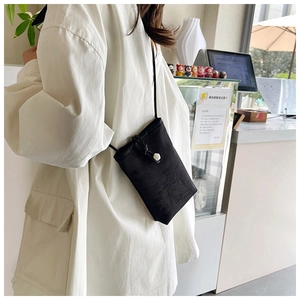 Detail of black embroidered mini crossbody bag with drawstring and white bead accent