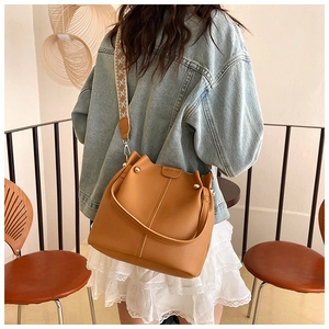 Detail of tan pebble leather bucket bag with wide geometric embroidery shoulder strap