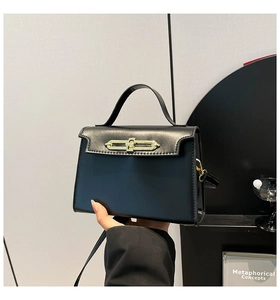 Detail of black trapezoid handbag with gold metal clasp and matte leather texture