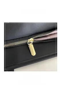 Close-up of golden metal zipper hardware on black leather tote bag with pink lining