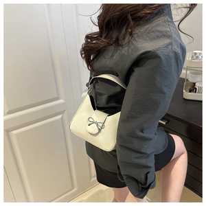 Model wearing a cream hobo shoulder bag with a silver bow decoration and long strap