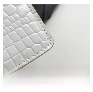 Detail of white patent leather with crocodile embossing and premium stitching on bag corner