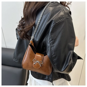 Brown leather underarm bag with silver bow and chain strap worn by a female model