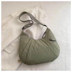 Detail view of sage green nylon crescent bag with wide strap and zip on corduroy