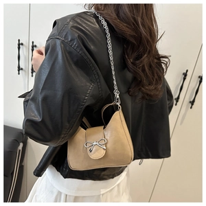 Detail of silver bow buckle and metallic chain on apricot leather underarm shoulder bag