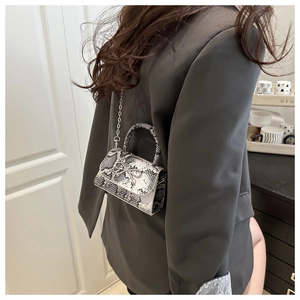 Detail of snake skin texture mini bag with silver bow buckle worn on shoulder