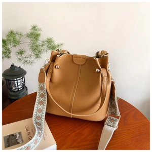 Close-up of caramel lychee grain leather bucket bag with retro geometric woven strap