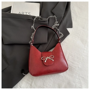 Detail of red textured leather handbag with silver metal bow and elegant chain strap
