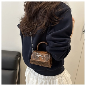 Brown crocodile pattern mini bag with silver bow detail and chain strap worn by a model